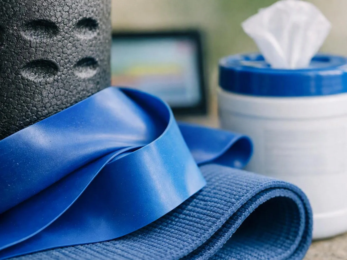 Blue and black workout mats and a resistance band sit beside a white wipe container with a tissue sticking out