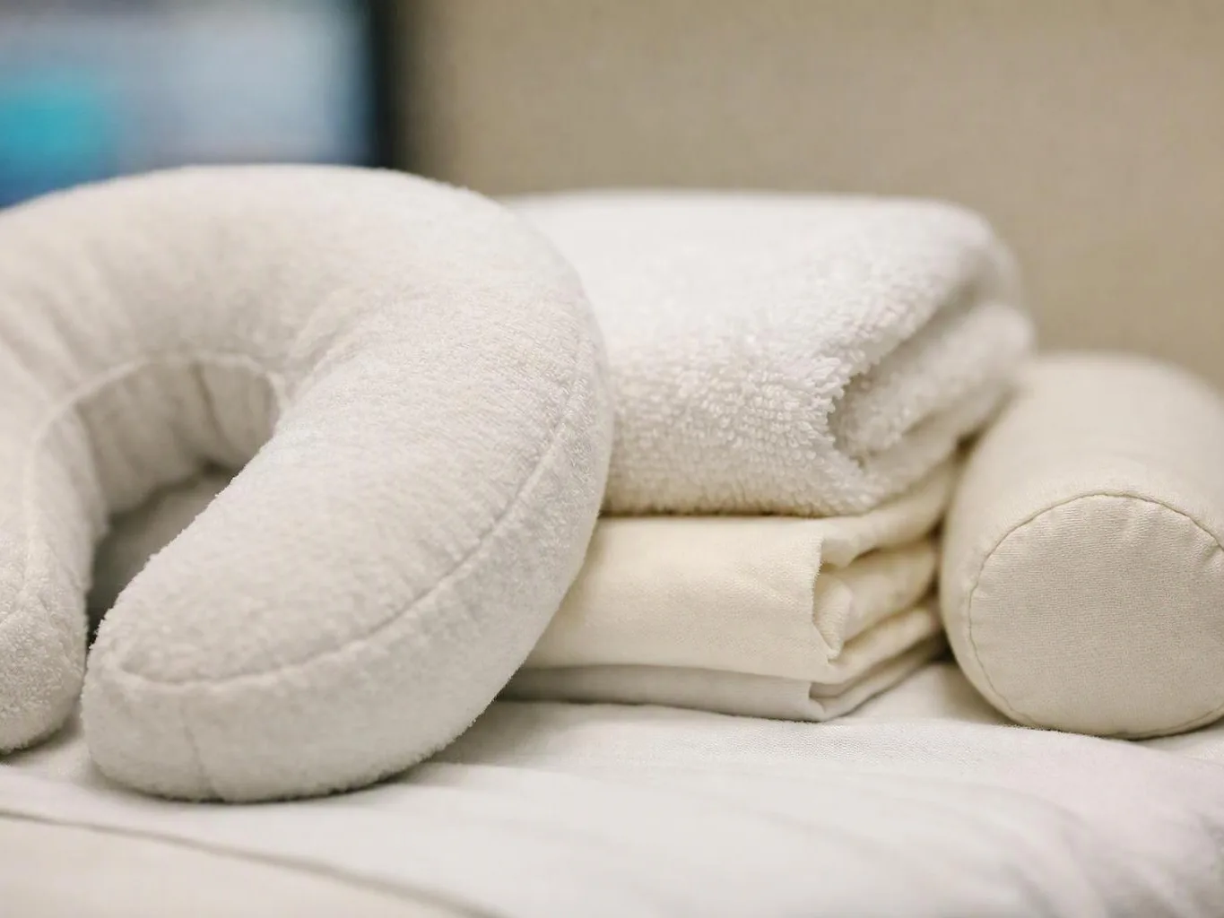 Rolled white towels and a neck pillow rest on a neatly made bed